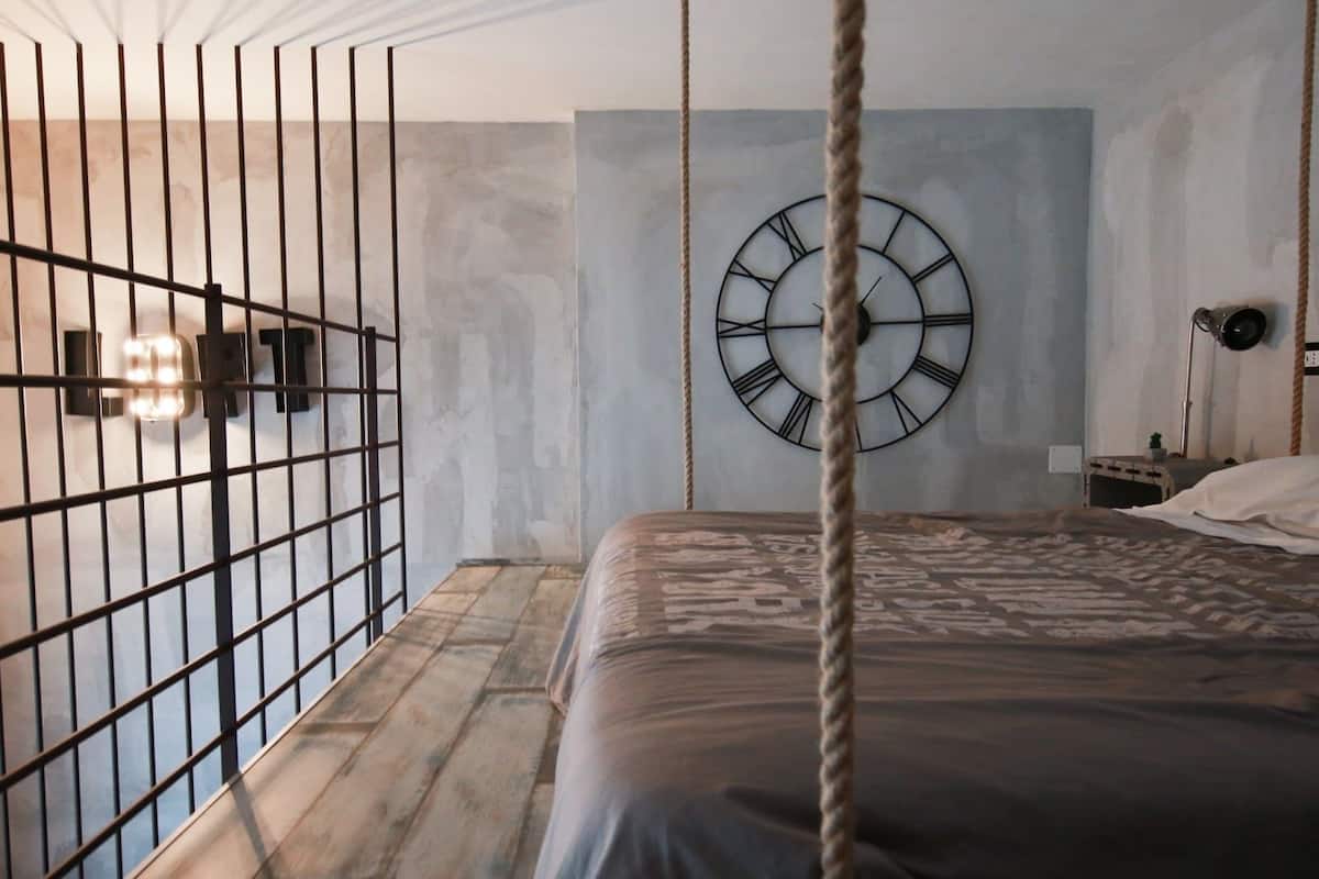 A bedroom with a bed, a wall clock, a rope, and a metal gate.