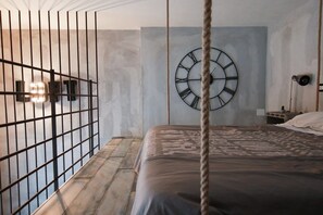 Un dormitorio con una cama, un reloj de pared, una cuerda y una reja de metal.