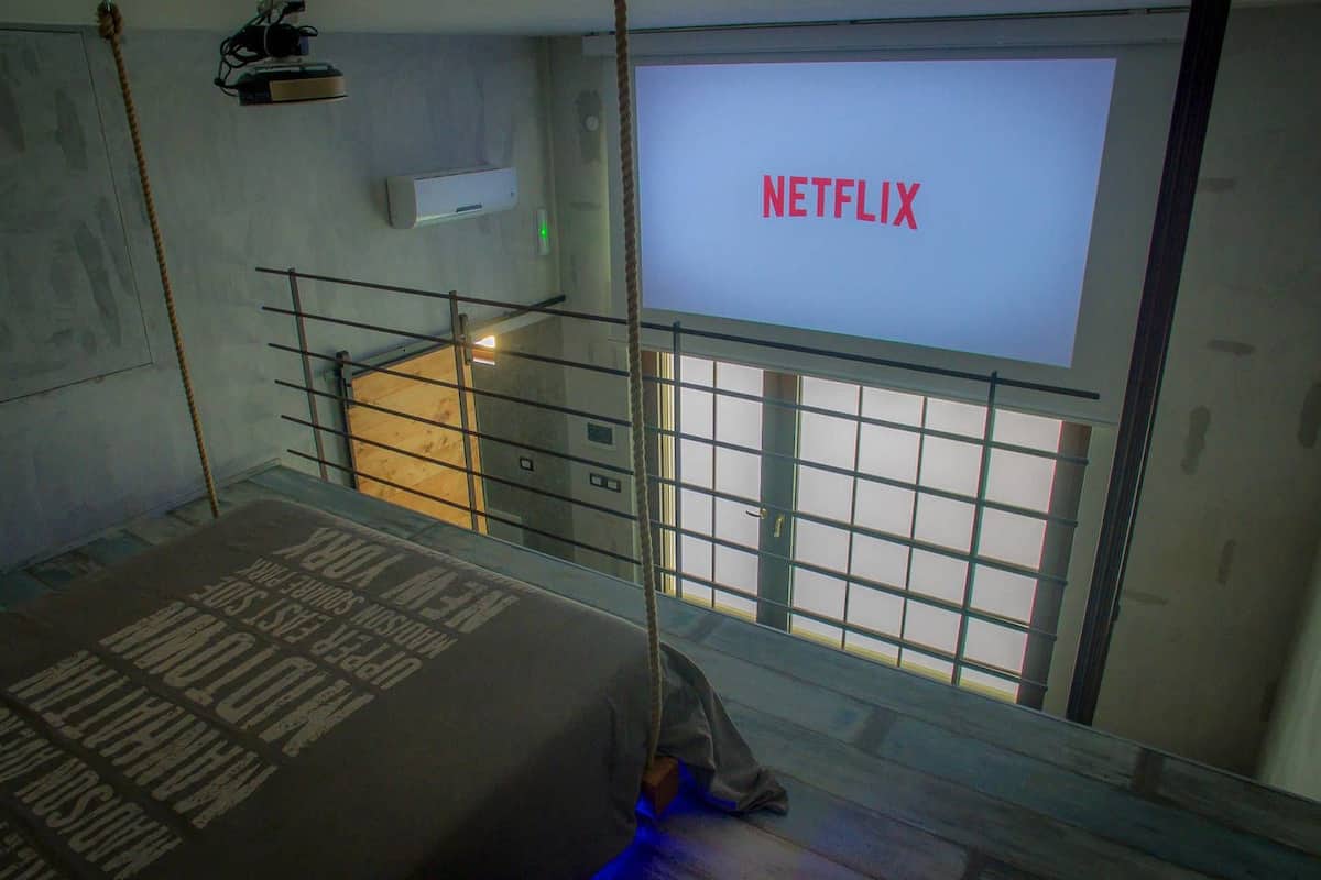 A room with a bed, a window, and a wall-mounted screen displaying "NETFLIX".