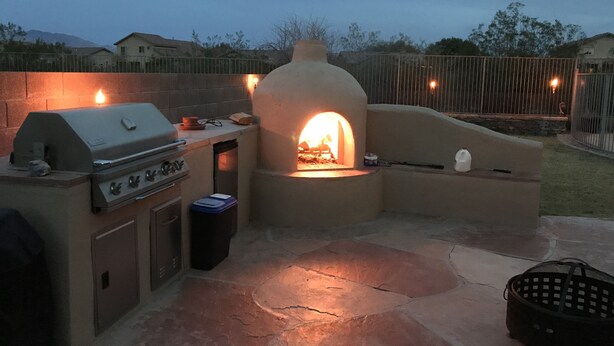 Cozinha externa com churrasqueira e forno, cercada por um pátio de pedra.