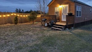 A wooden cabin with a porch, a small deck, and a string of lights. - Mountain Views | Fire Pit | little bear cabin (Island Park)