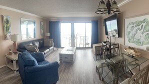 A living room with a sofa, a glass coffee table, a dining table with chairs, a TV, and artwork on the walls. - August Hot Summer Special On The Beach!! 199nt. Disc for August ..Pet Friendly! (Destin)