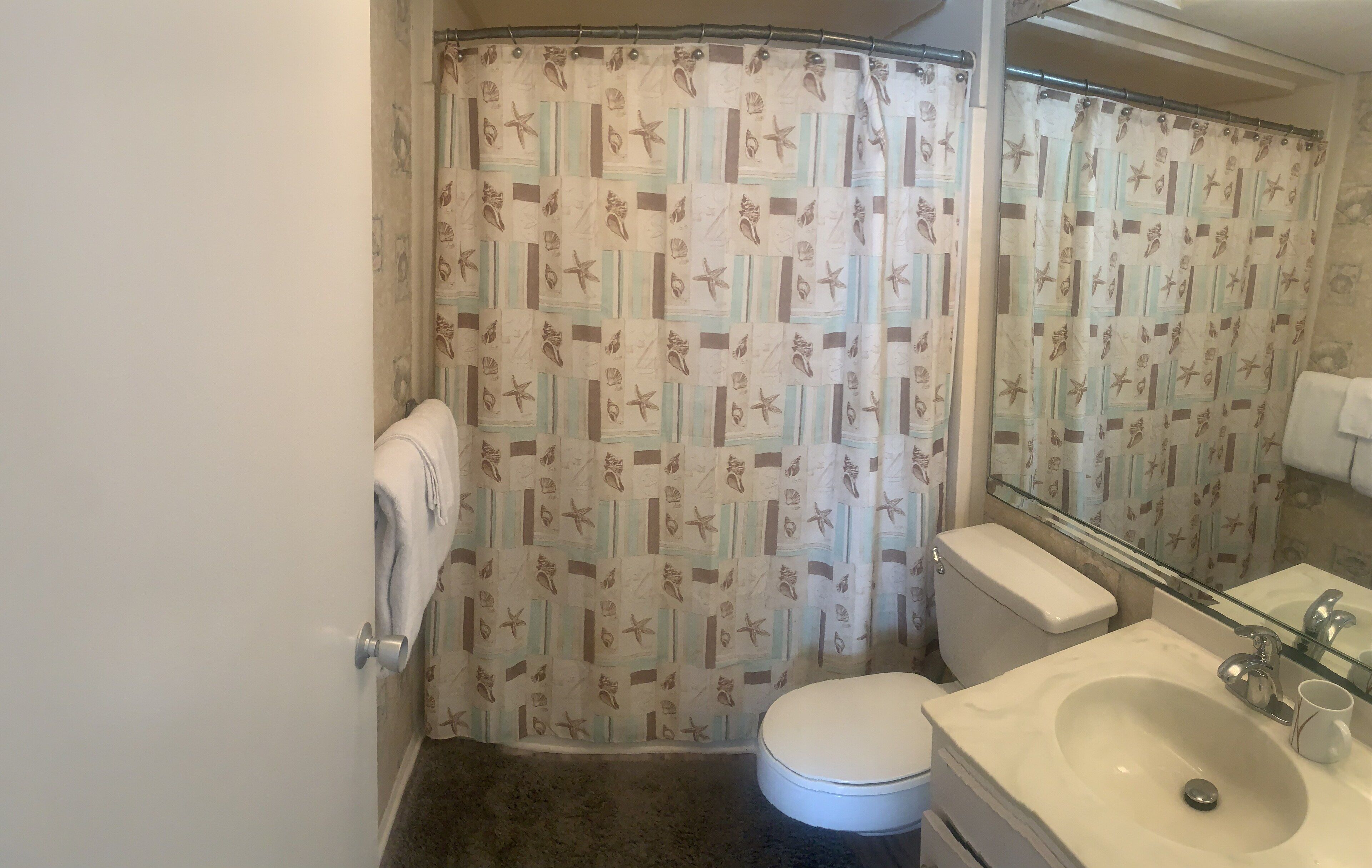 A bathroom with a shower curtain featuring a nautical pattern, a toilet, a sink with a mirror, and a towel rack.