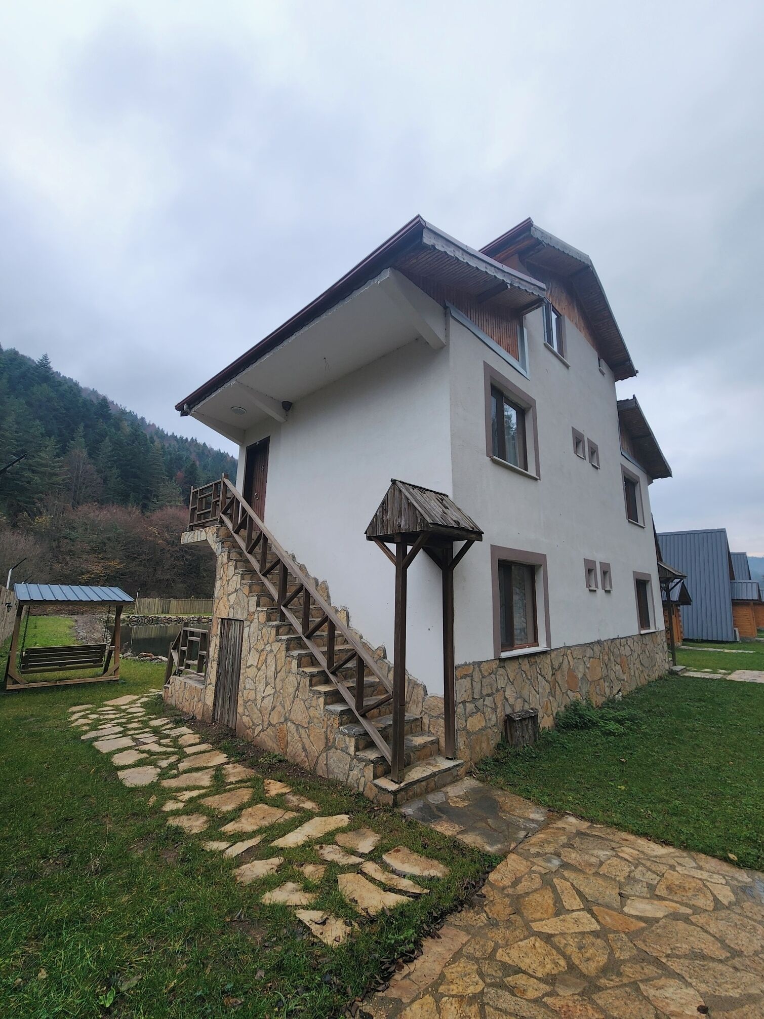 A two-story house with a stone foundation, a wooden staircase, and a small porch.