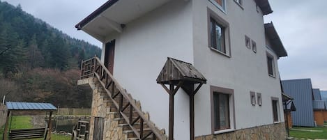 A two-story house with a stone foundation, a wooden staircase, and a small porch.