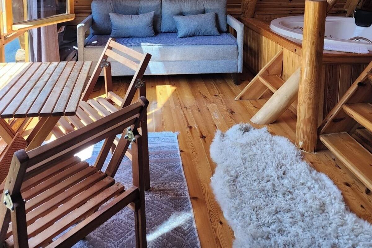 Interior acolhedor de uma cabana de madeira, com sofá, mesa pequena e ofurô.