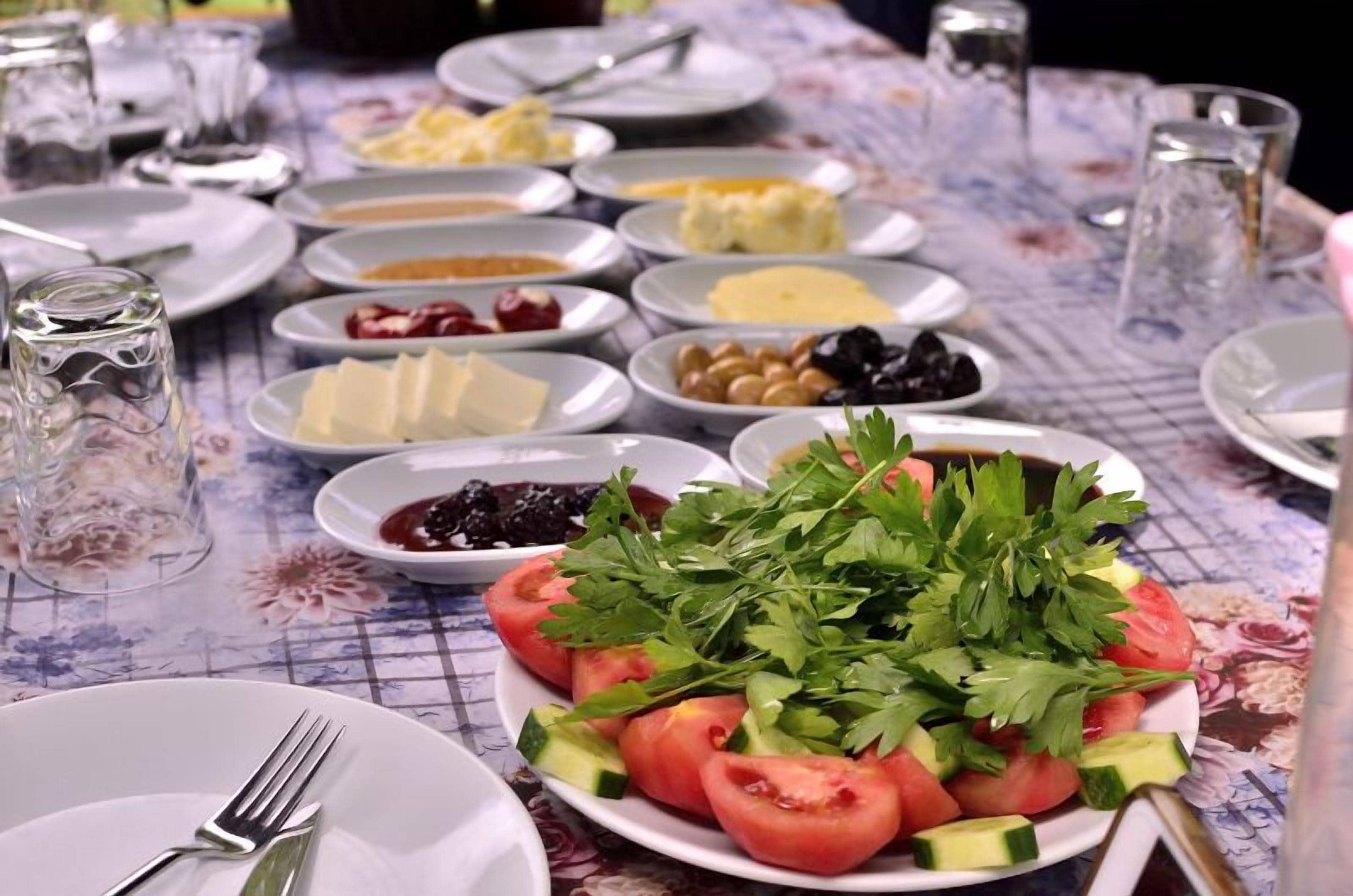 A table set with various dishes including a salad with tomatoes and cucumbers, olives, and cheese.