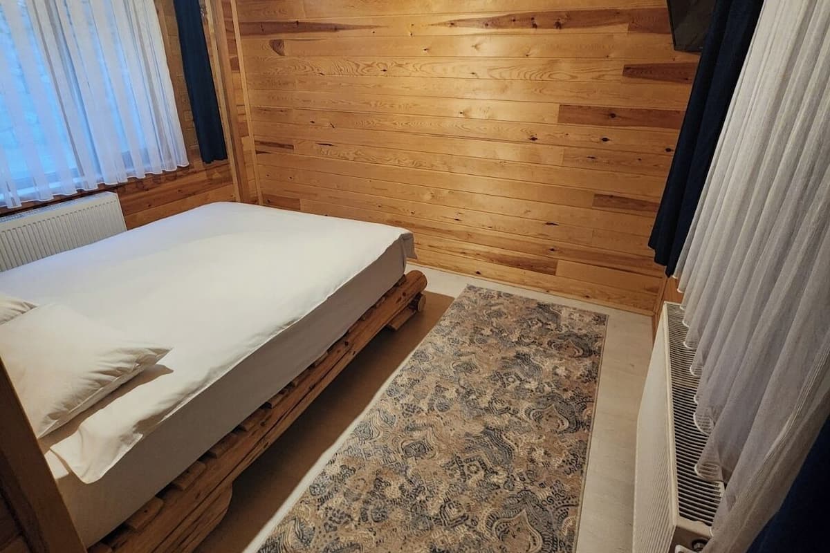 Um quarto com painéis de madeira, uma cama, um tapete estampado e um lustre.