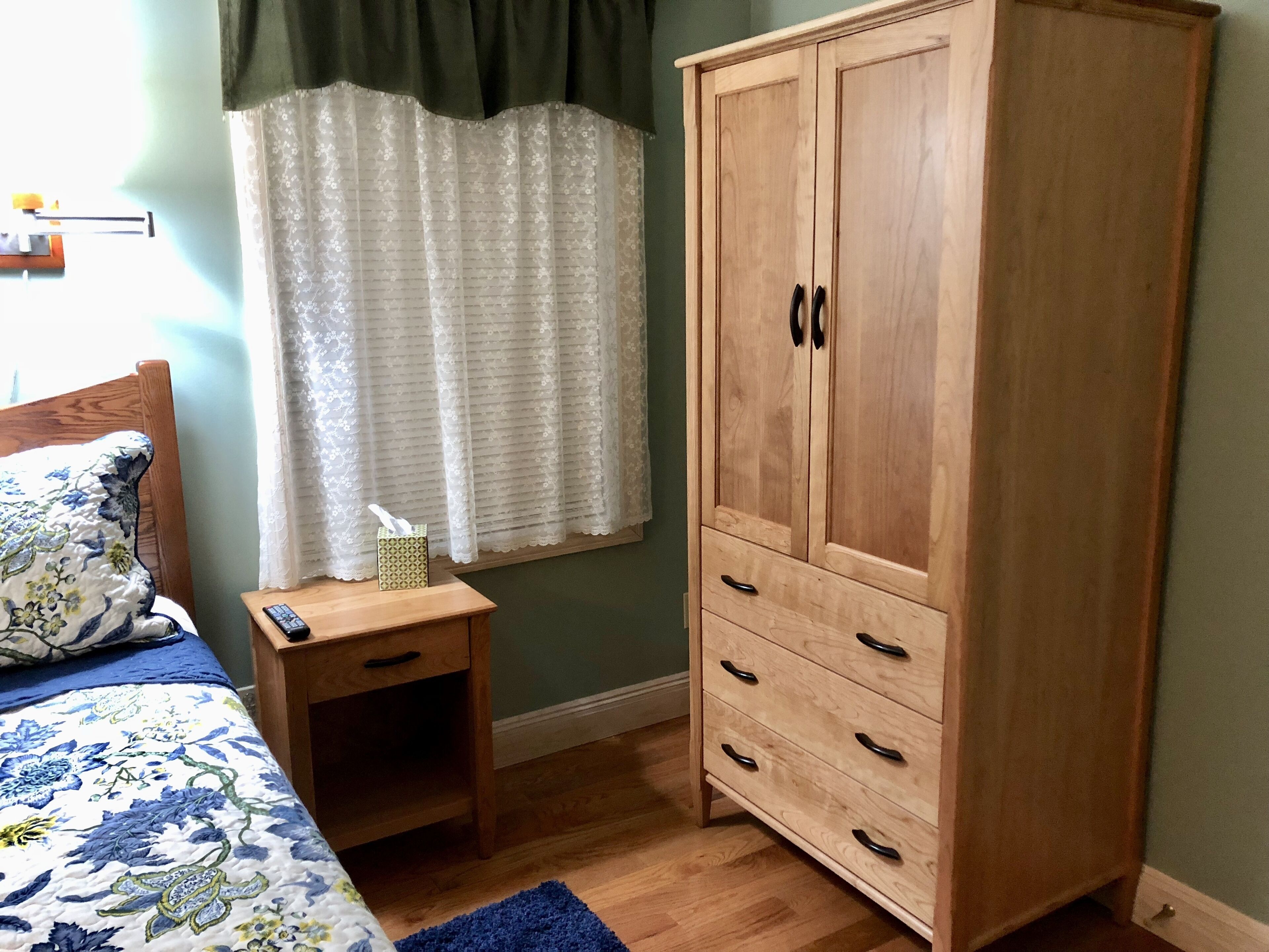 A bedroom with a wooden wardrobe, a bedside table with a remote control, and a floral bedspread.