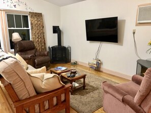 A living room with a fireplace, a television mounted on the wall, and a comfortable seating area with a sofa and armchairs. - Immaculate Hummingbird Suite - One Mile from Acadia National Park (Bar Harbor)