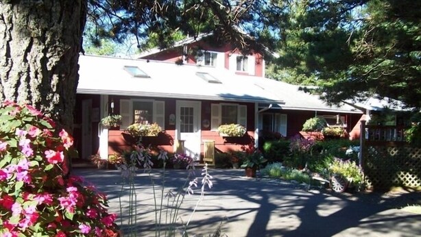 Una casa de fachada roja, con porche delantero y jardín lleno de plantas y flores.