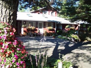 A house with a red facade, a front porch, and a garden with various plants and flowers. - Immaculate Hummingbird Suite - One Mile from Acadia National Park (Bar Harbor)