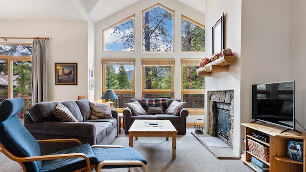 A spacious living room with a fireplace, large windows, and a television. - Waterdance 475a 5 Bedroom Townhouse by RedAwning (Frisco)