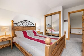 Een slaapkamer met een houten bed, nachtkastje, spiegel en kledingkast.