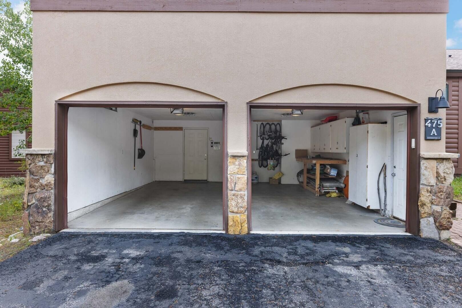 A garage with two arched entrances, a stone wall, and a sign indicating the address.