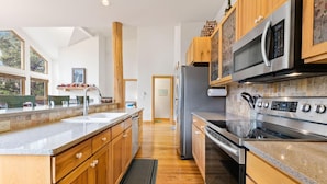 A modern kitchen with wooden cabinets, stainless steel appliances, and a large window providing natural light. - Waterdance 475a 5 Bedroom Townhouse by RedAwning (Frisco)