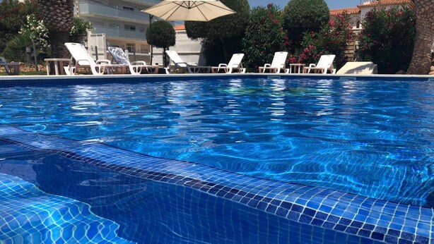 A swimming pool with clear blue water, surrounded by lounge chairs and umbrellas.