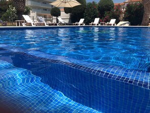 Una piscina con agua azul cristalina, rodeada de sillones de descanso y sombrillas.