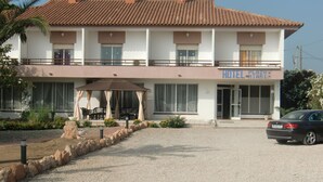 A two-story hotel with a tiled roof, a covered outdoor seating area, and a car parked in front.