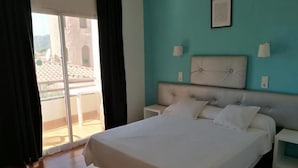 A bedroom with a large bed, a view through a sliding door to an outdoor area, and a teal-colored wall.