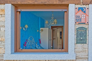 Una ventana con vista a una habitación que tiene una pared azul, un candelabro y una cama con flores rosadas.