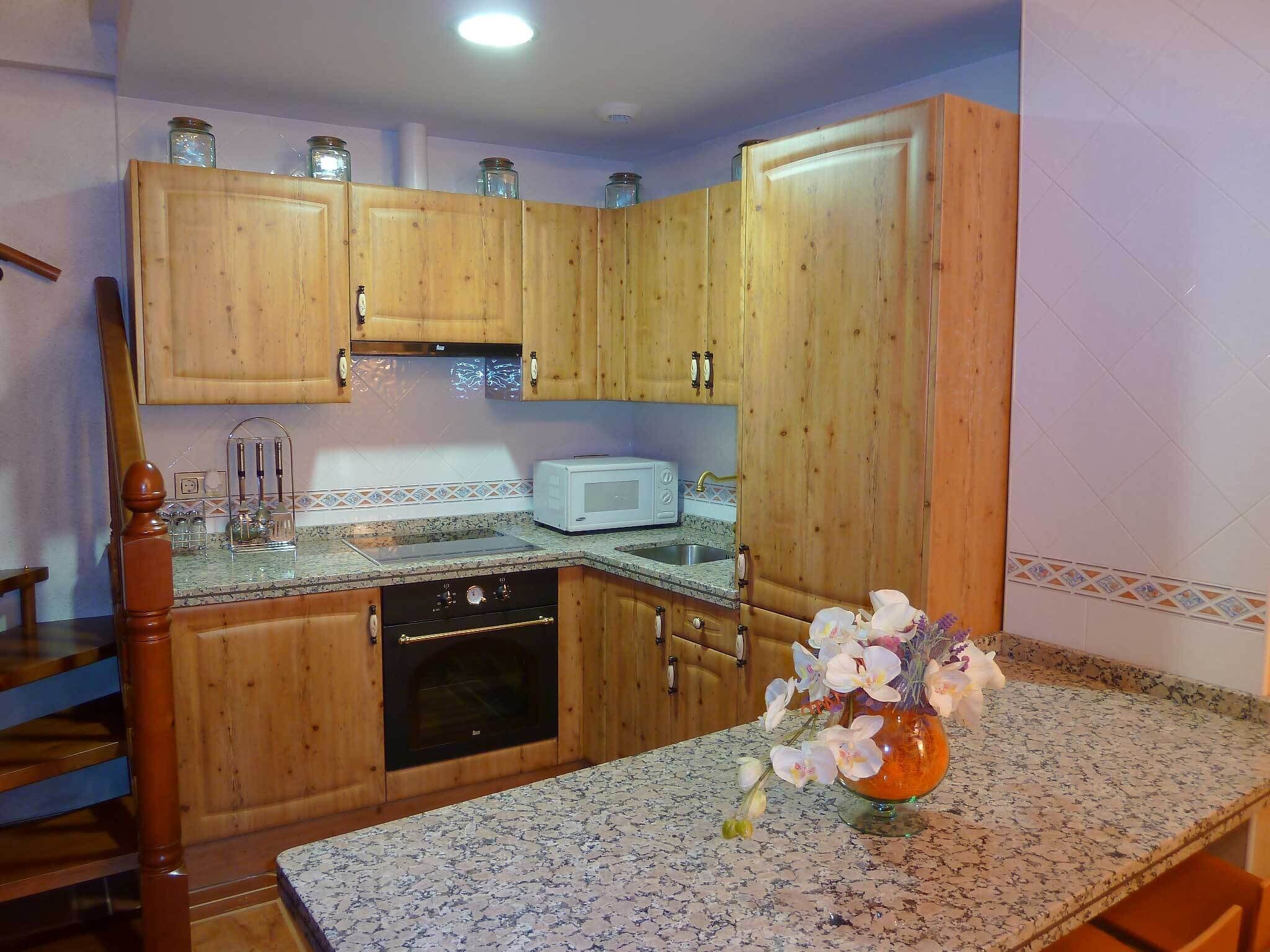 A kitchen with wooden cabinets, a microwave, a dishwasher, and a vase with flowers on the countertop.