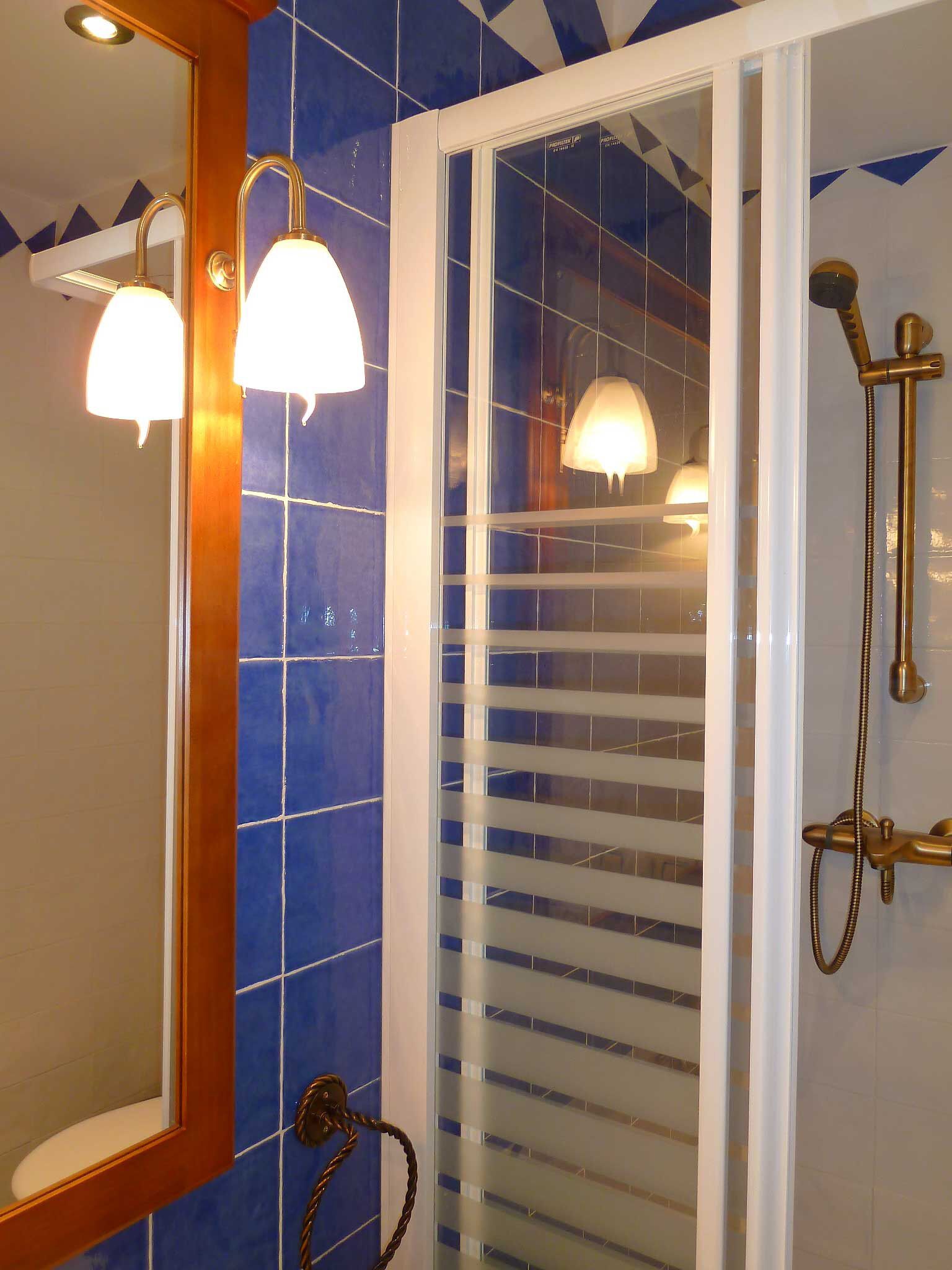 Un baño con azulejos azules, una puerta blanca y una ducha con cabezal dorado.