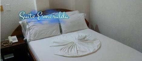 A hotel room with a neatly made bed, a bedside telephone, and a sign indicating the room name 'Suite Esmeralda'.