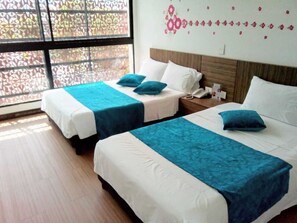 A hotel room with two beds, each with a blue bedspread and white linens. There is a window with a view of a lattice fence outside. - Suite Sumapaz Hotel (Melgar)