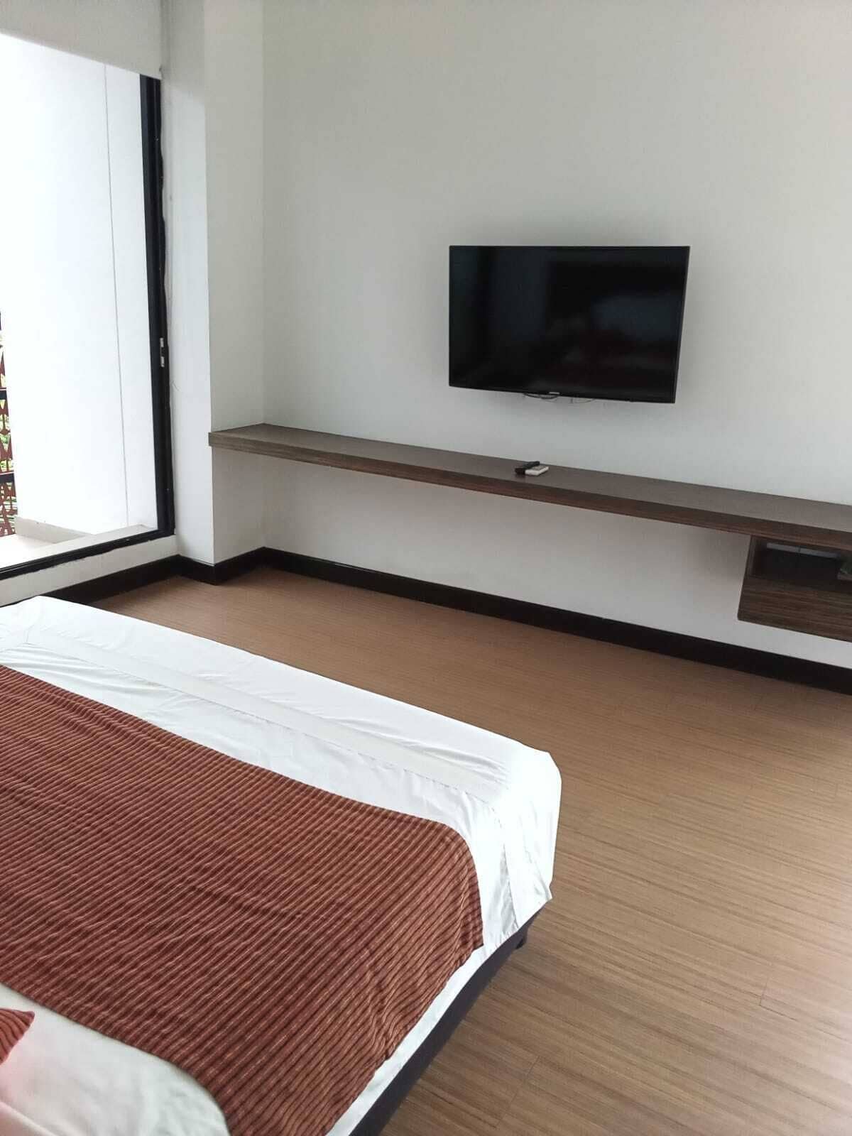 A hotel room with a bed, a TV mounted on the wall, and a window with a view.