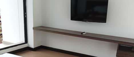 A hotel room with a bed, a TV mounted on the wall, and a window with a view.