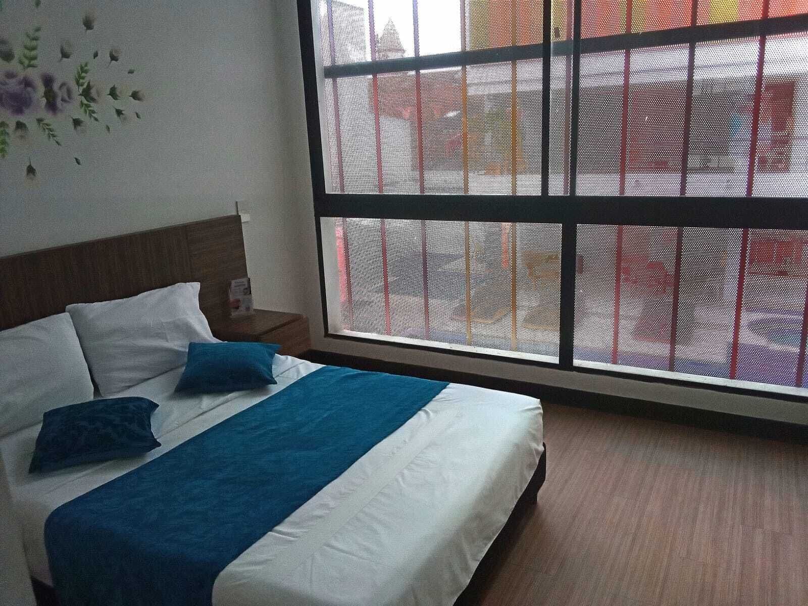 A hotel room with a large window, a bed with white and blue bedding, and a wooden headboard.