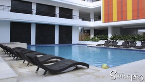 A swimming pool with lounge chairs, a basketball court, and a view of the hotel building. - Suite Sumapaz Hotel (Melgar)