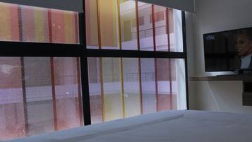 A hotel room with a bed, a TV mounted on the wall, and a window with a red and yellow patterned blind.