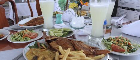 A dining table with various dishes including fried fish, fries, and salads, along with two glasses of a light-colored beverage.