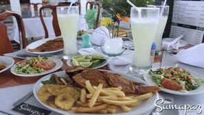 A dining table with various dishes including fried fish, fries, and salads, along with two glasses of a light-colored beverage. - Suite Sumapaz Hotel (Melgar)