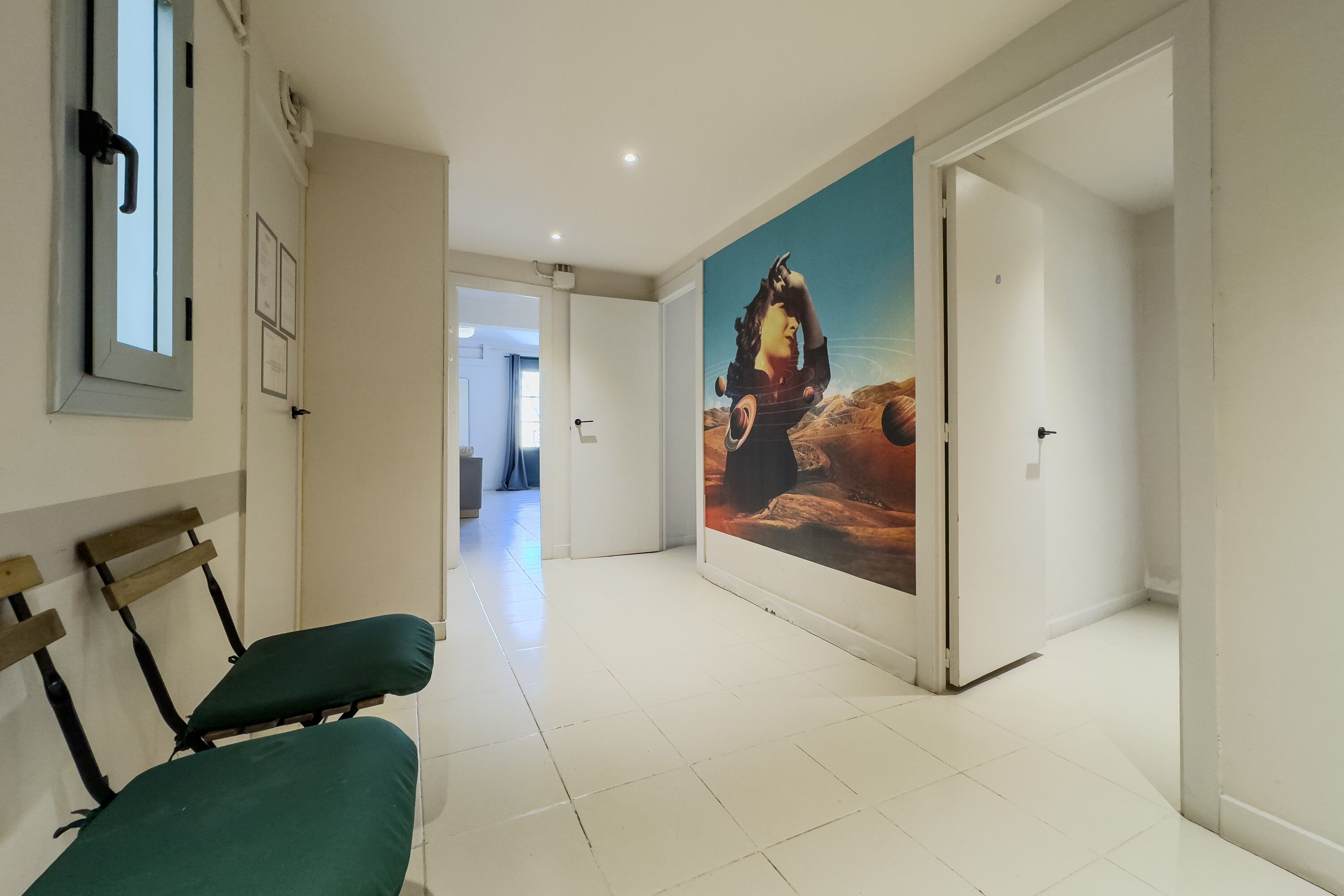 A hallway with a green cushioned bench, a large mural on the wall, and a door leading to another room.