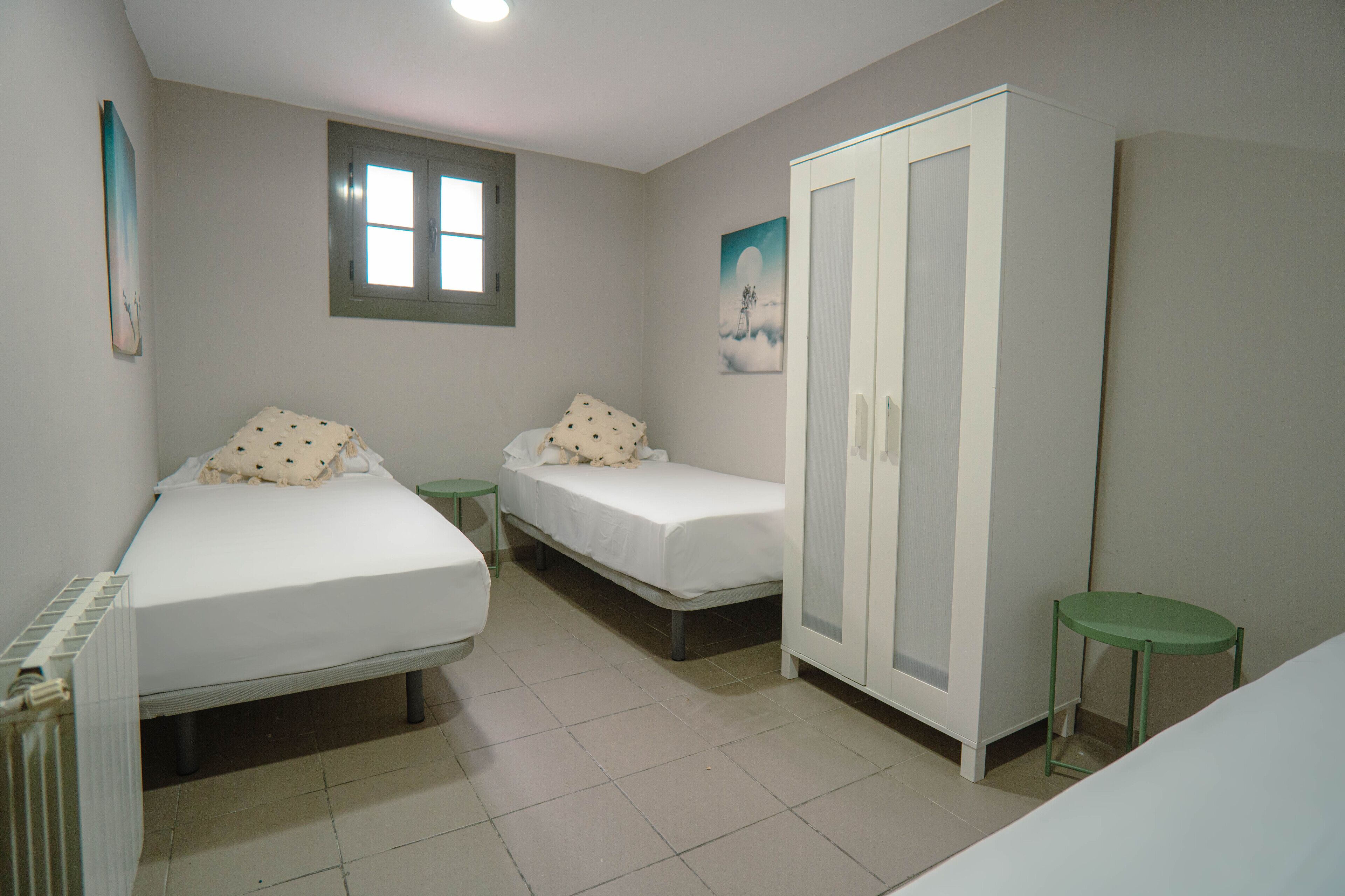 Een slaapkamer met twee eenpersoonsbedden, een kledingkast, een radiator en een raam.