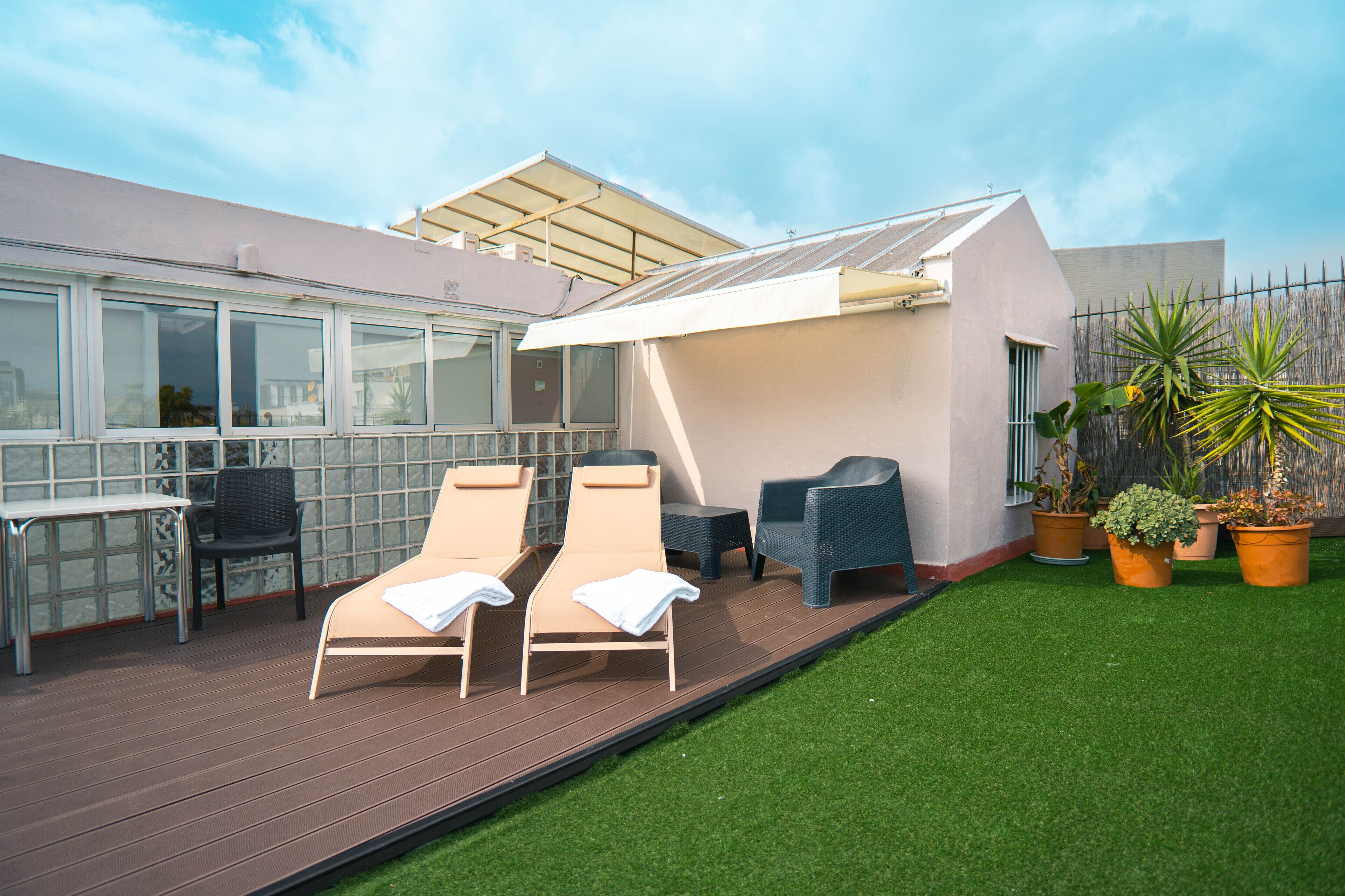 A rooftop lounge area with two lounge chairs, a table, and potted plants.
