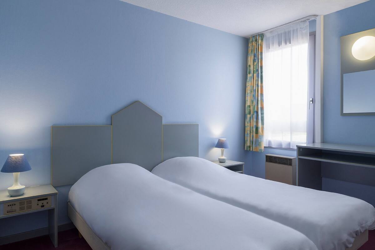 A hotel room with a bed, bedside tables, a desk, a mirror, and a window with curtains.