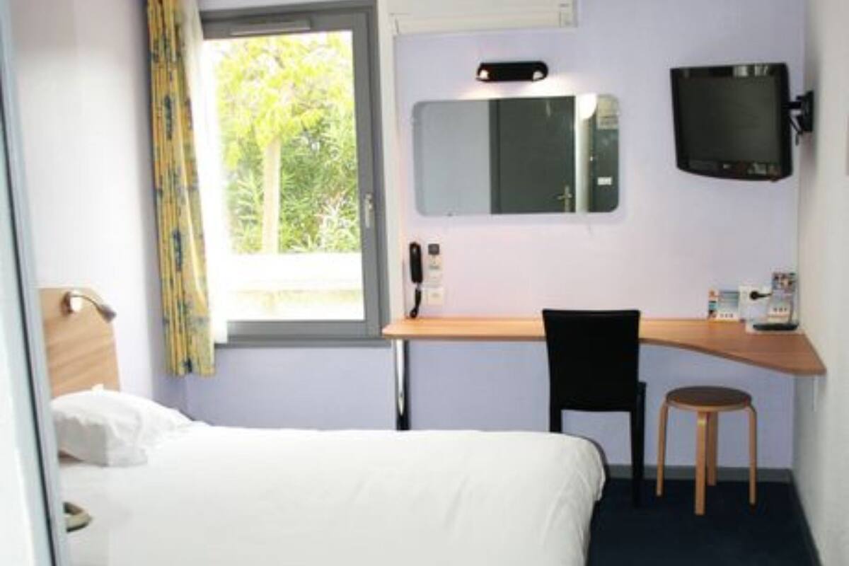 A hotel room with a bed, a desk, a chair, a television, and a window with curtains.