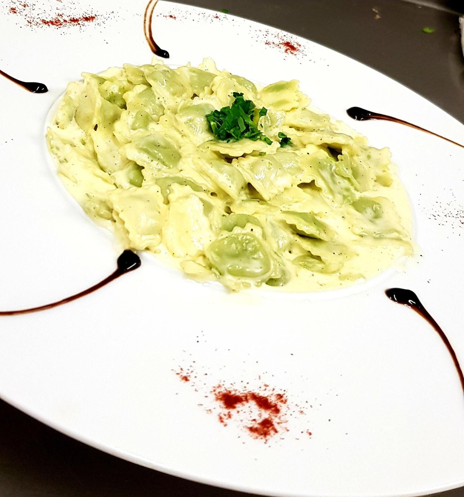A plate of pasta with a garnish, served on a white plate with decorative lines and red specks.