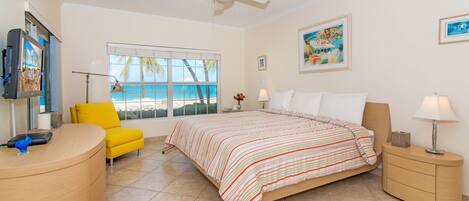A hotel room with a bed, a desk, a chair, a window with a view of the beach, and a ceiling fan.