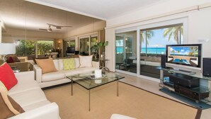 A modern living room with a glass coffee table, white sofas, and a television. - The Colonial Club, Oceanfront Condos (Seven Mile Beach)