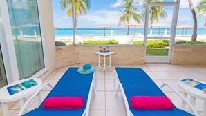 A balcony with two sun loungers, a table with a hat, and a view of the beach and ocean. - The Colonial Club, Oceanfront Condos (Seven Mile Beach)