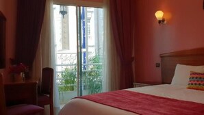 A hotel room with a bed, a desk, a chair, a window with curtains, and a wall-mounted light fixture. - Hotel Amouday (Casablanca)