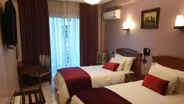 A hotel room with two beds, a chair, a desk, and a window with curtains. - Hotel Amouday (Casablanca)