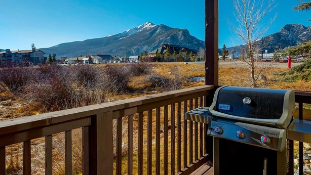 Une terrasse en bois équipée d’un barbecue Weber Spirit, offrant une vue sur un paysage montagneux parsemé de maisons et d’une végétation clairsemée.