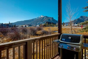 Une terrasse en bois équipée d’un barbecue Weber Spirit, offrant une vue sur un paysage montagneux parsemé de maisons et d’une végétation clairsemée.