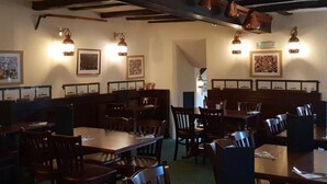 Un restaurante con mesas y sillas de madera, cuadros en las paredes y lámparas colgantes.